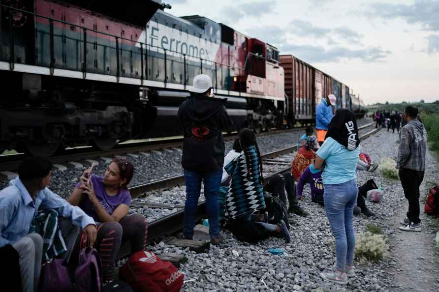 Migrants watch a train go past as they wait along the train tracks...