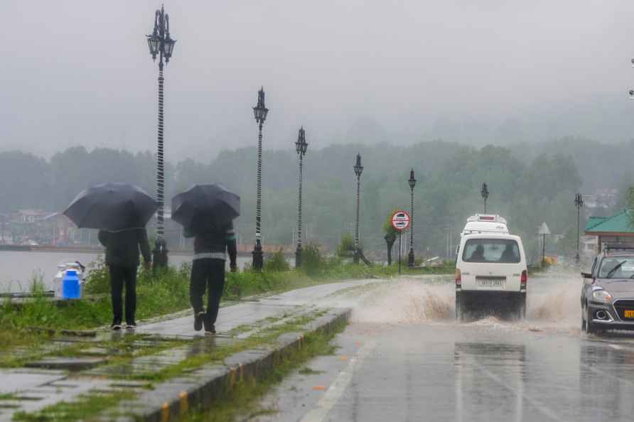 Srinagar: People, holding umbrellas, walk along a road during rains...